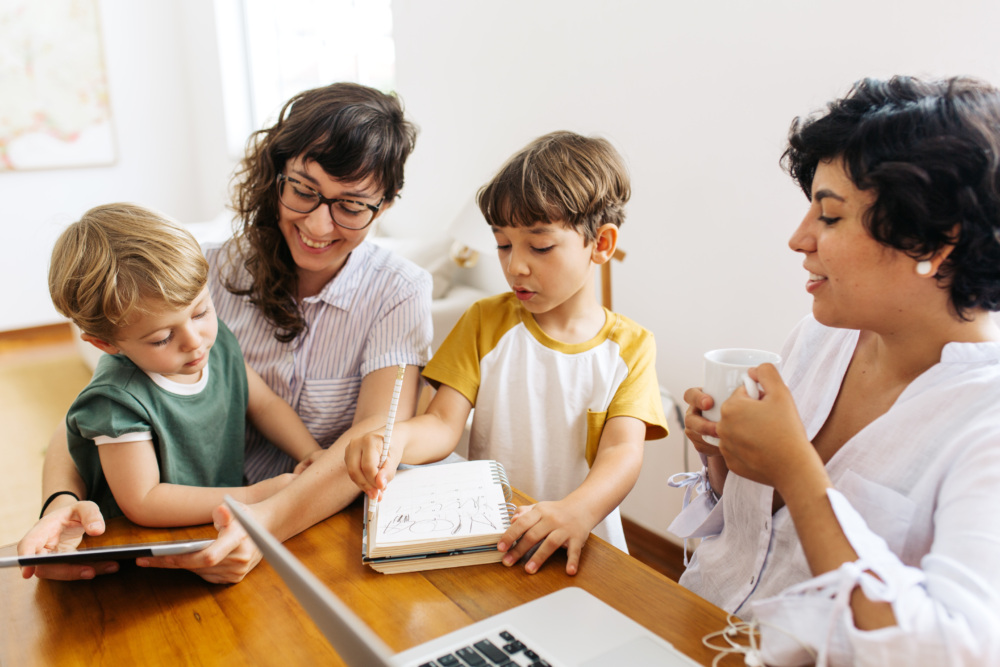Lesbian couple sitting with their kids using a digital tablet.