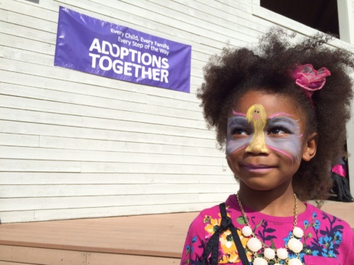 Child wearing facepaint stands in front of a sign at fall family day