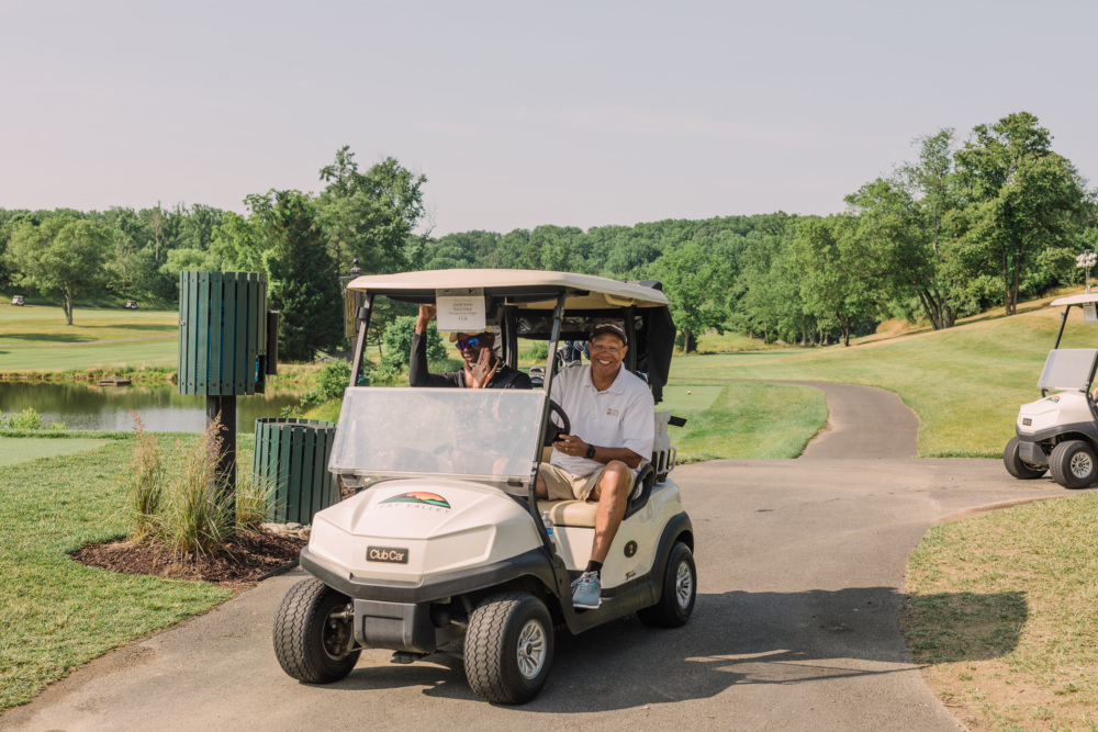 Duo smiling as they drive a golf cart at Swing Into Action for Kids, Paths for Families' annual golf tournament