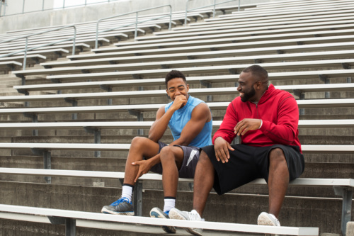 Older man mentoring young teenager. They laugh as they sit together on bleachers