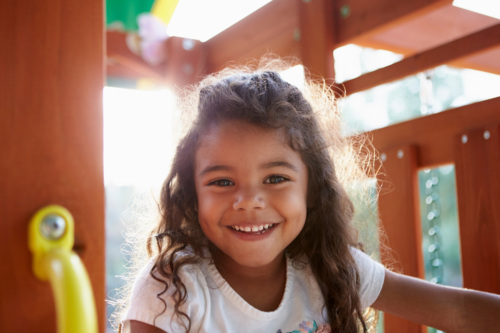 A young girl happily plays on a playground and smiles at the camera