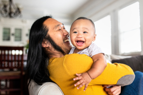 Asian American Father Hugging His Young Child As They Smile