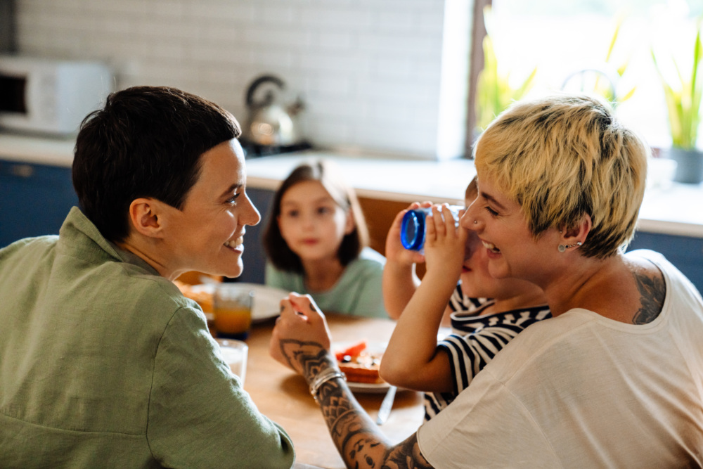Lesbian couple sits at a table with their two young children