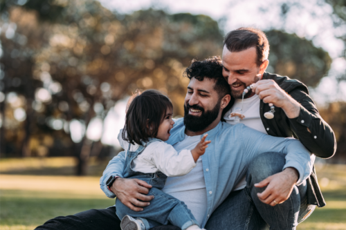 Two dads spending time playing with their daughter at the park