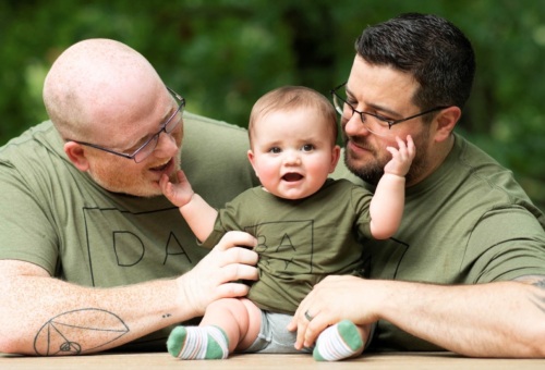 Two dads smile with their baby