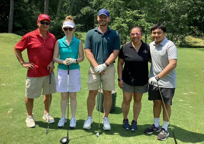 A group of five people pose for a smile at an annual golf tournament