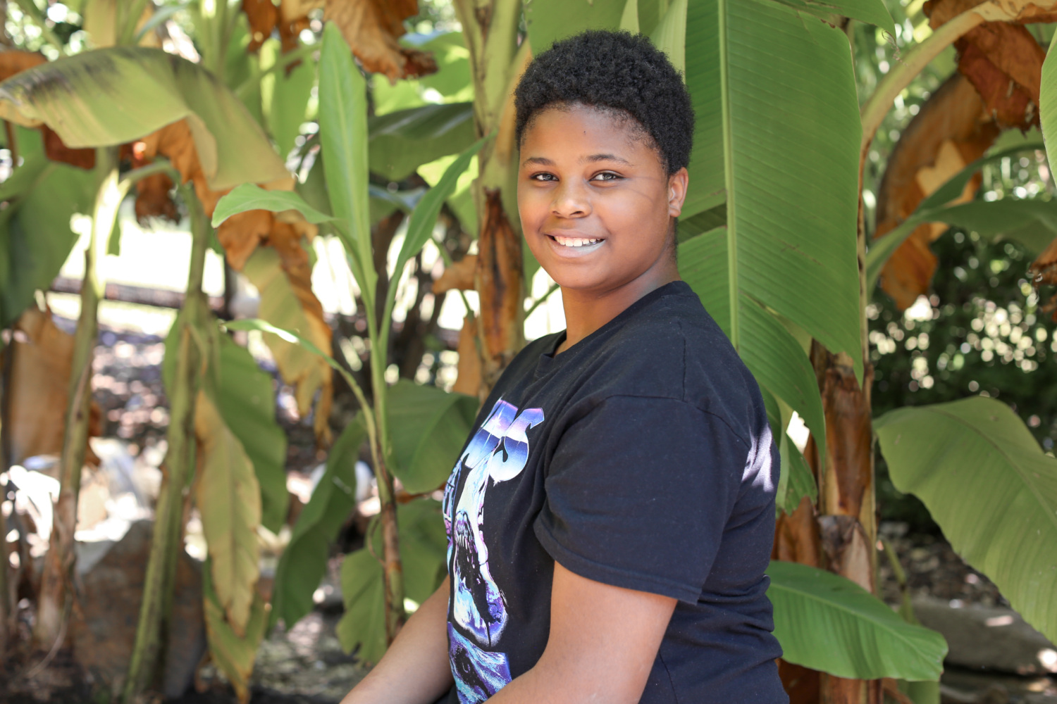 A young girl smiling as she stands among some large plants