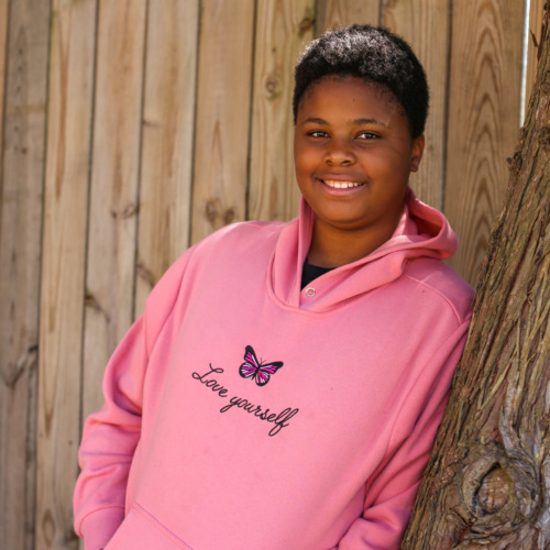 Young girl smiling in a pink sweatshirt as she leans against a tree