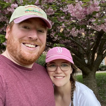 A couple smiles in front of a cherry blossom tree