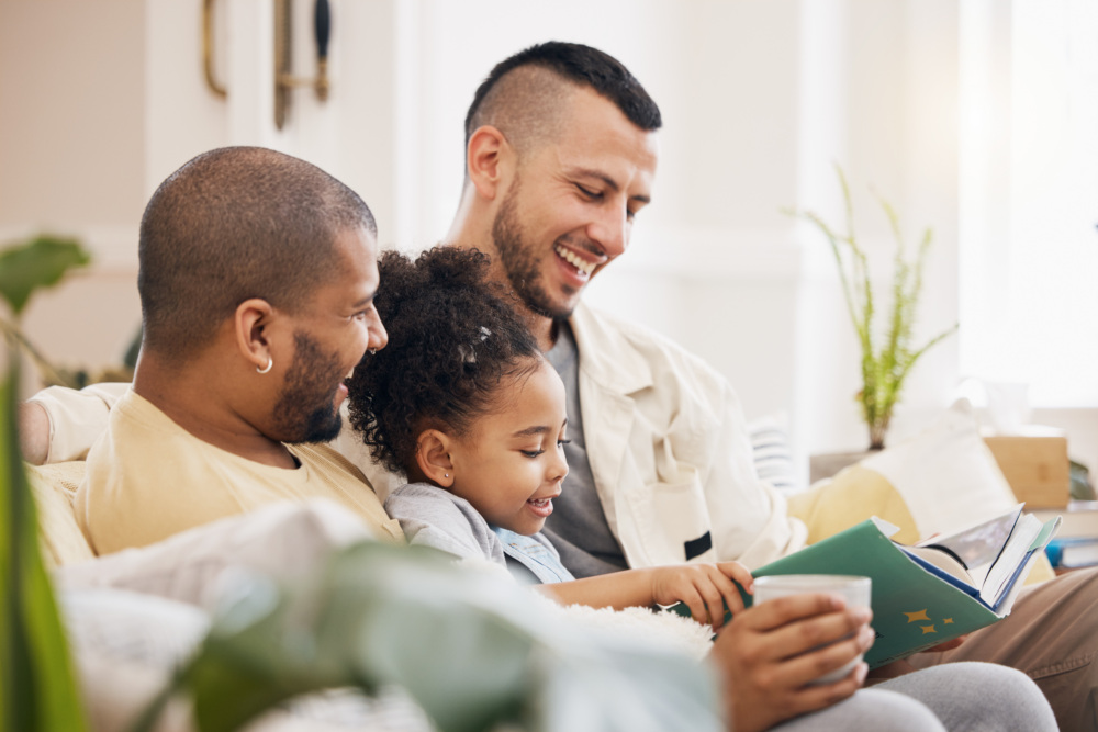 A couple sits on the couch, reading with their daughter